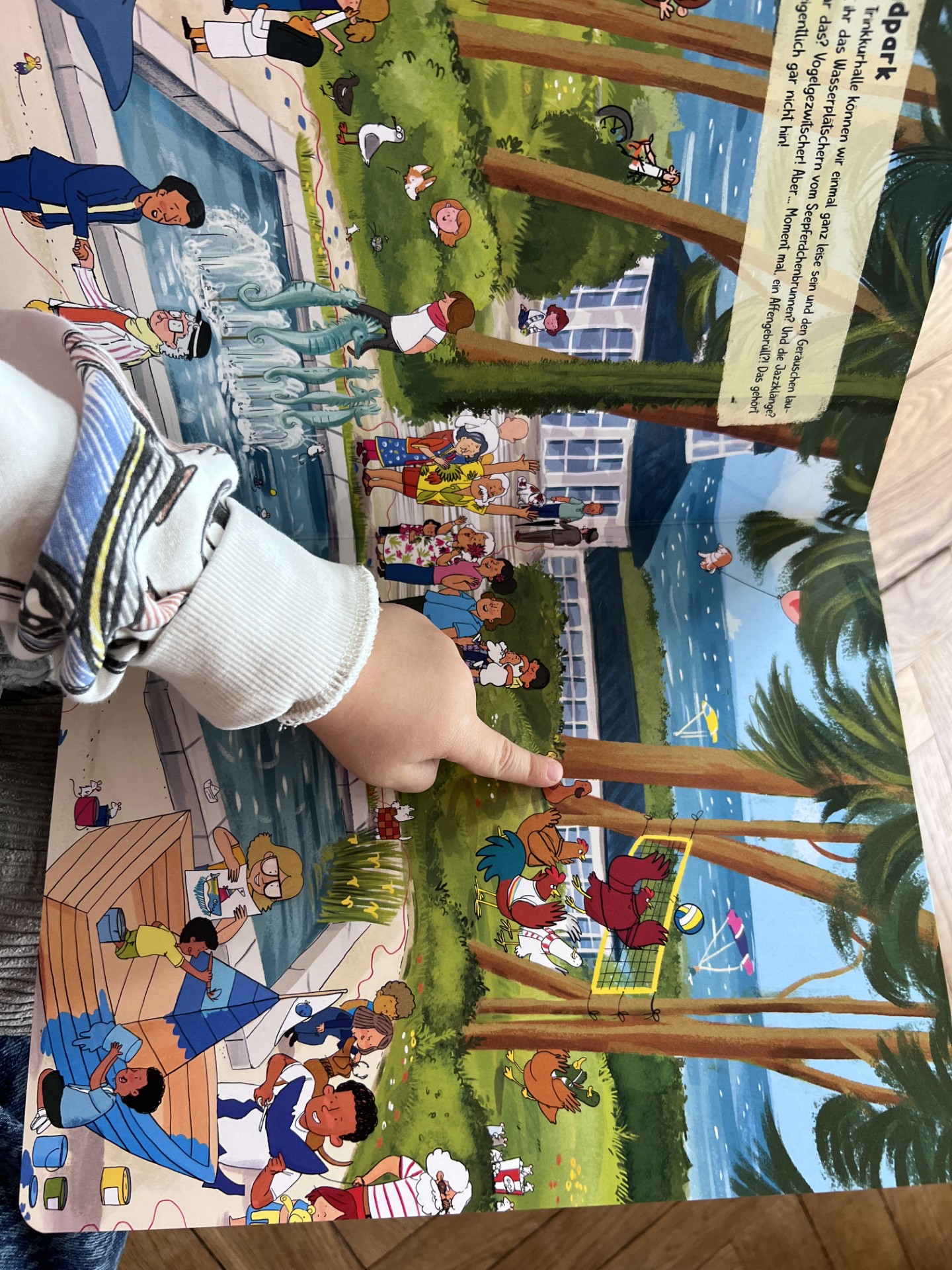 Eine Kinderhand zeigt auf eine Figur im Wimmelbuch. 