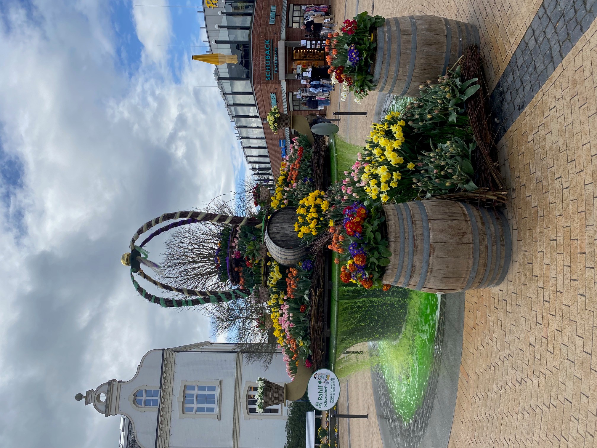 Bunt bepflanzter Osterbrunnen und im Hintergrund das alte Rathaus von Timmendorfer Strand