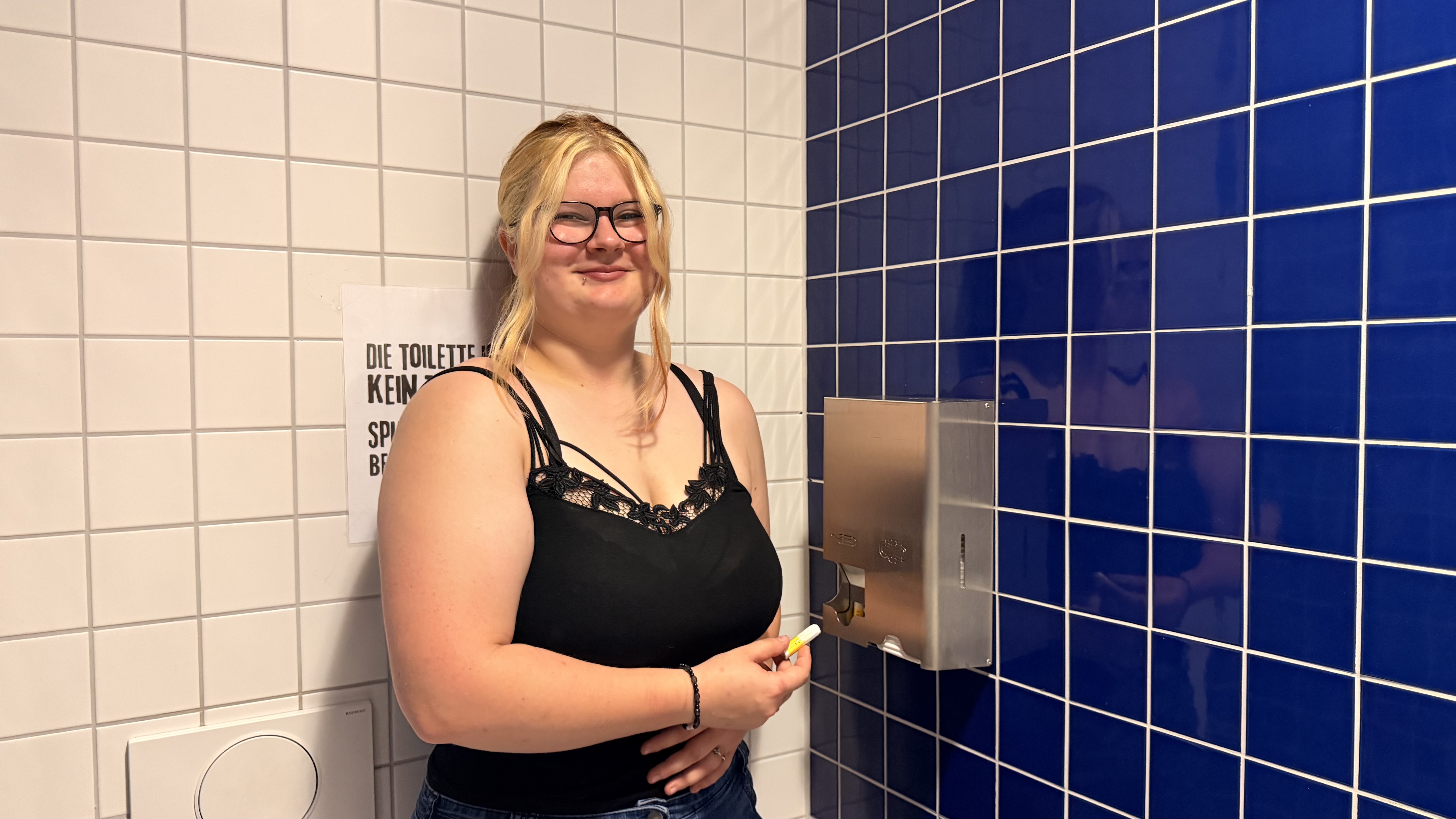 Ein Mädchen, was neben einem Spender steht und die ein Tampon in der Hand hält