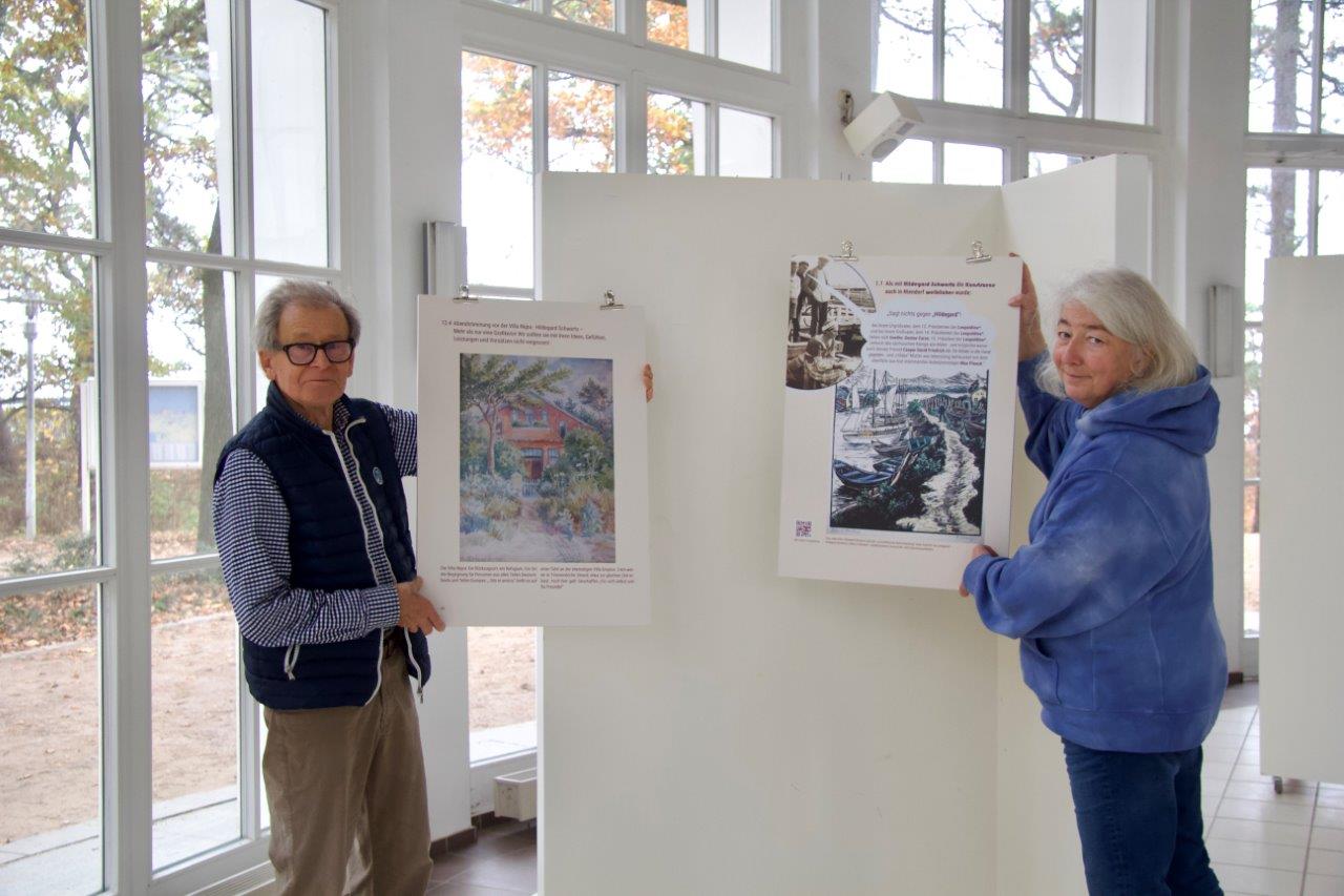 Ein Mann und eine Frau präsentieren zwei Kunstwerke in einem Ausstellungsraum