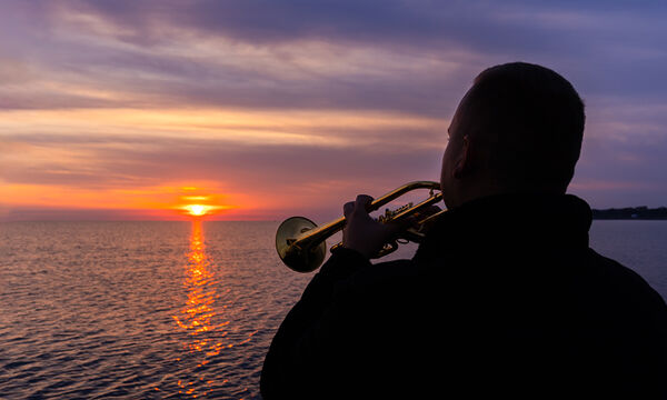 Mann mit Trompete beim Sonnenaufgang auf der Ostsee
