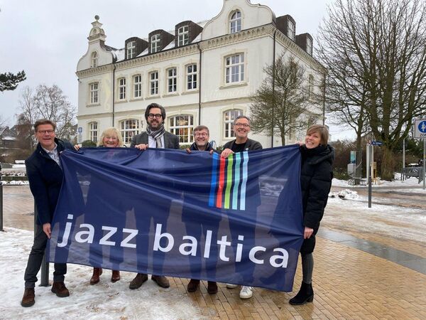Sechs Menschen mit einem Banner mit dem Schriftzug Jazz Baltica in der Hand vor einem alten Gebäude