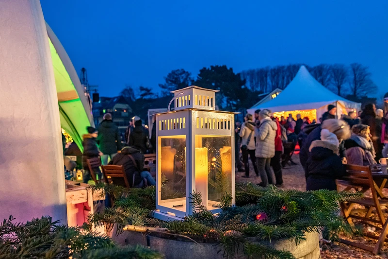 Nahaufnahme einer Kerze in einer Laterne im Hintergrund sieht man Menschen auf dem Weihnachtsmarkt