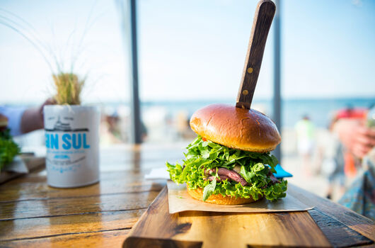 Burger auf einem Brett vor dem Ausblick auf einen Strand