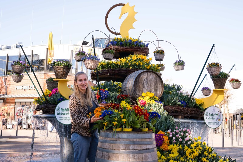Lara Klewin steht vor einem bunt geschmückten Osterbrunnen. 