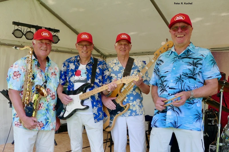 Vier alte Herren in Hawaiihemden mit Instrumenten und roten Kappen auf