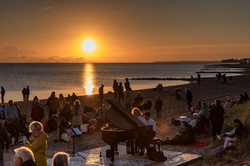 Menschen genießen gemeinschaftlich den Sonnenaufgang am Niendorfer Freistrand