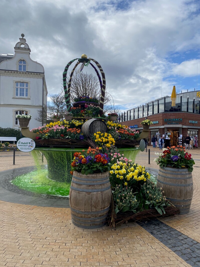 Bunt bepflanzter Osterbrunnen und im Hintergrund das alte Rathaus von Timmendorfer Strand