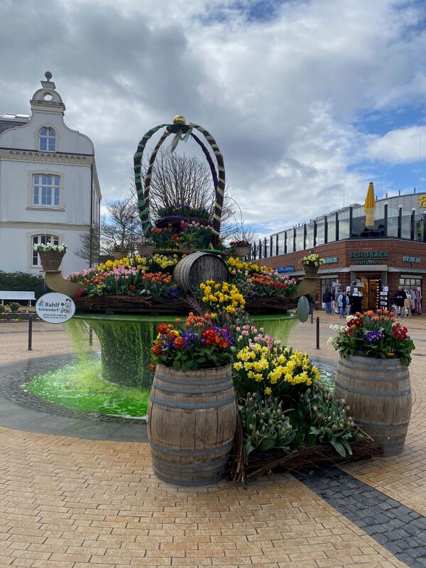 Bunt bepflanzter Osterbrunnen und im Hintergrund das alte Rathaus von Timmendorfer Strand
