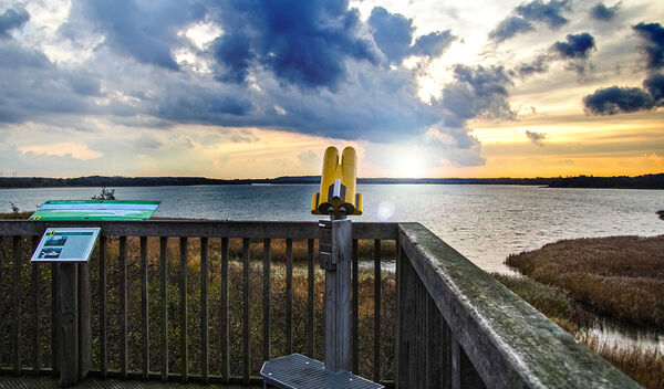 Ein Geländer und einfeststehendes Fernglas vor dem Sonnenuntergang über einem See