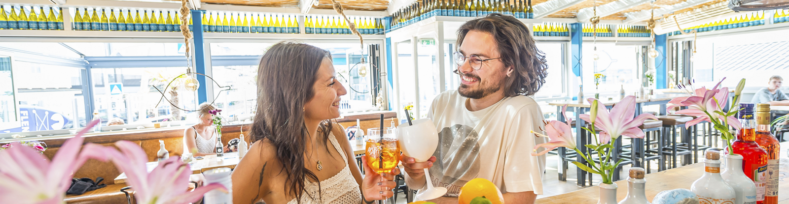Fröhliches Pärchen am Tresen eines Lokals stößt mit Weingläsern an