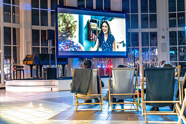 Menschen sitzen in Liegestühlen vor einer Leinwand und gucken einen Film