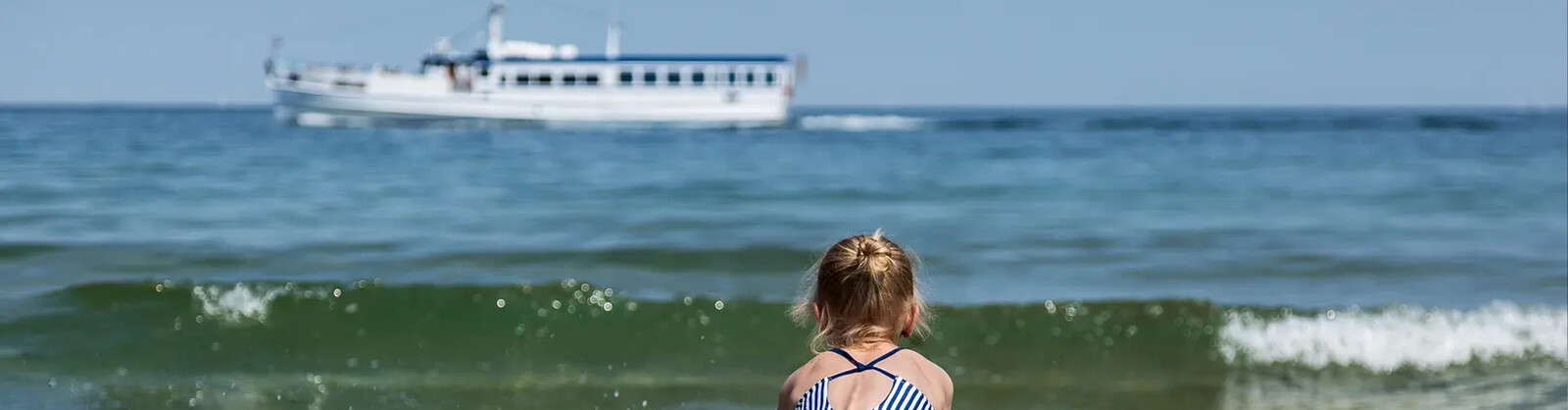 Kind am Strand und im Hintergrund ein Schiff