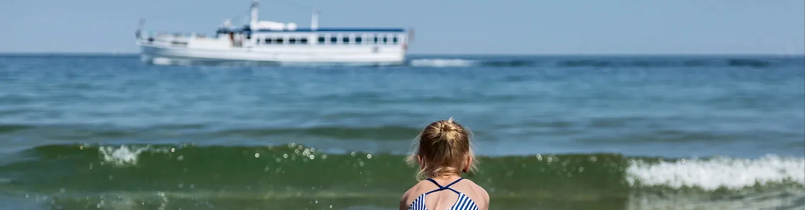 Kind am Strand und im Hintergrund ein Schiff