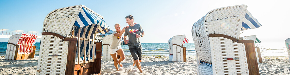 Pärchen spielt fangen zwischen Strandkörben am Strand