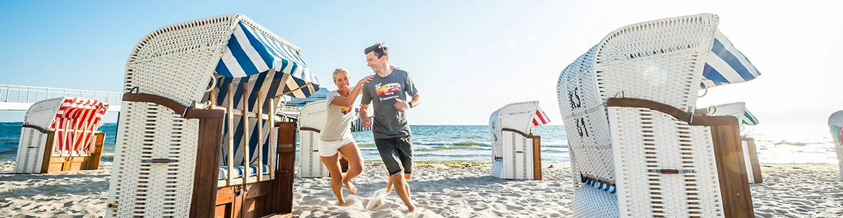 Pärchen spielt fangen zwischen Strandkörben am Strand