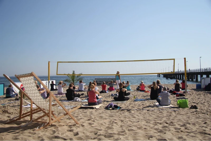 Eine Gruppe macht Yoga auf einem Beachvolleyballfeld