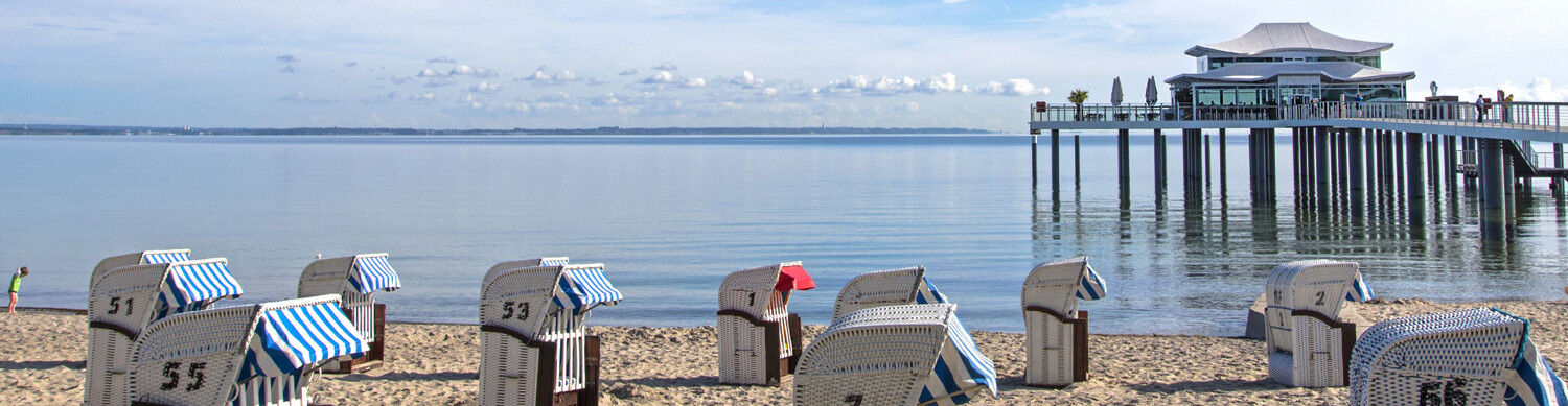 Strand mit einem asiatisch angehauchten Gebäude auf einem Steg um Hintergrund und Strandkörben im Vordergrund