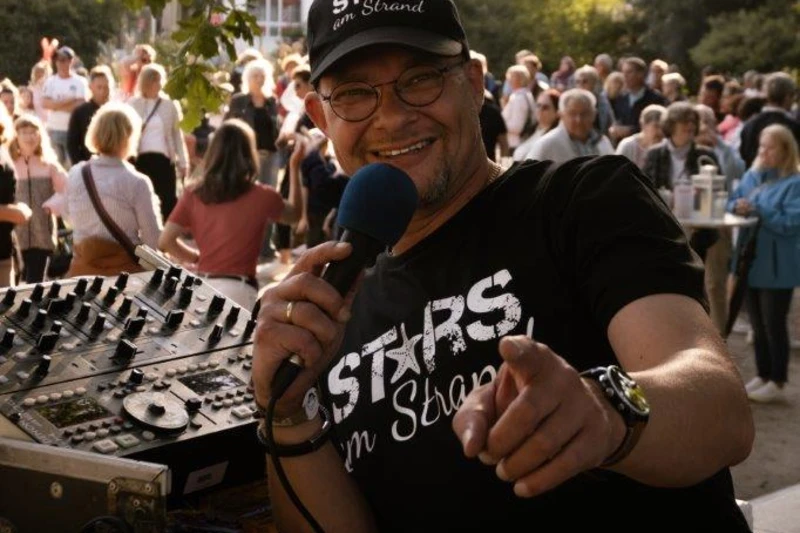 René Kleinschmidt mit einem Mikrofon in der Hand steht vor einer tanzenden Menschenmenge