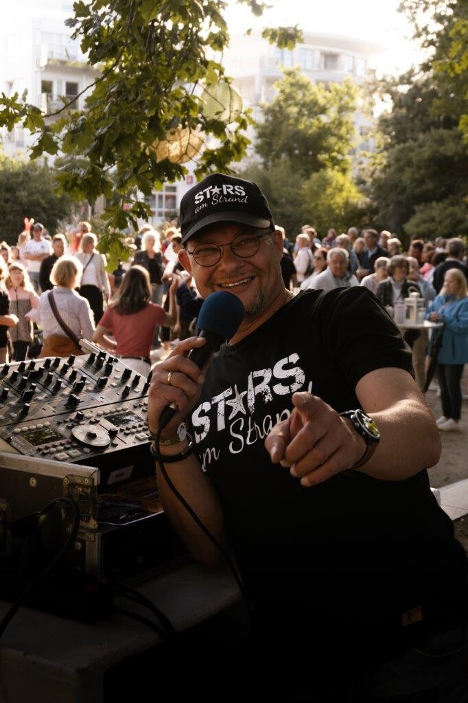 René Kleinschmidt mit einem Mikrofon in der Hand steht vor einer tanzenden Menschenmenge