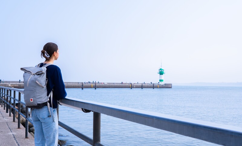 Cara schaut auf das Meer. Im Hintergrund ist ein grüner Leuchtturm.