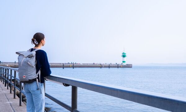 Cara schaut auf das Meer. Im Hintergrund ist ein grüner Leuchtturm.