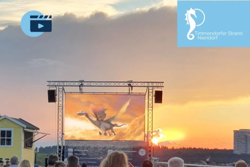 Viele Menschen schauen einen Film auf einer Leinwand am Strand im Abendrot
