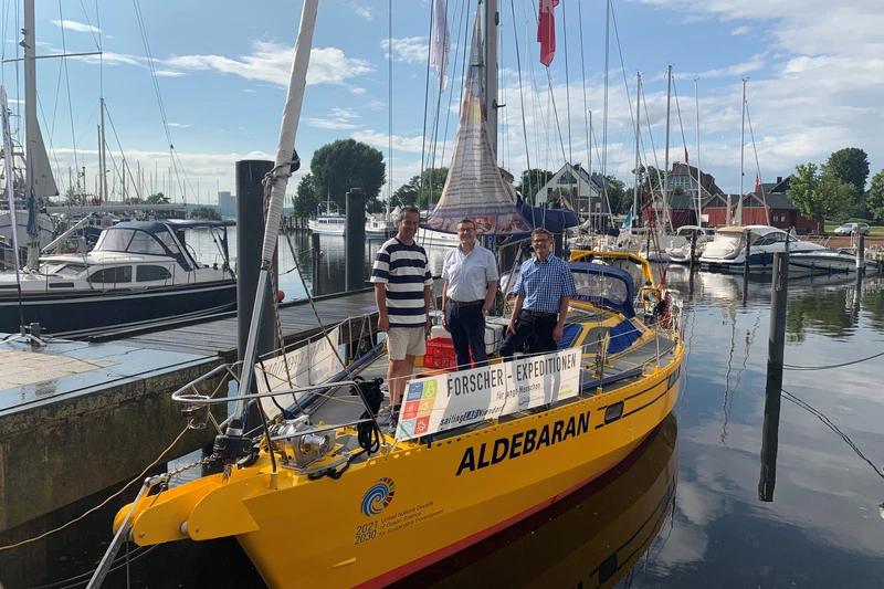 Das gelbe Forschungsschiff Aldebaran im Hafen mit drei Männern darauf