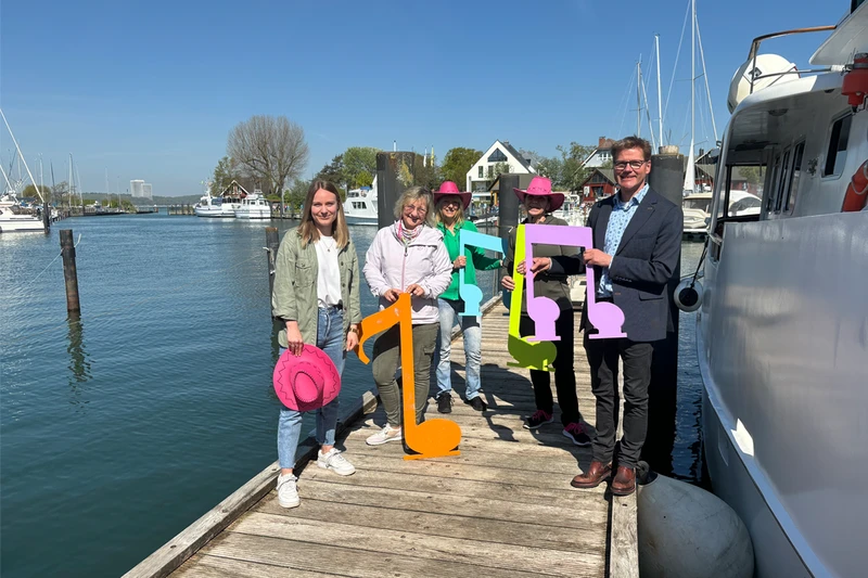 Eine Gruppe steht mit farbigen Noten in den Händen auf einem Bootsanleger