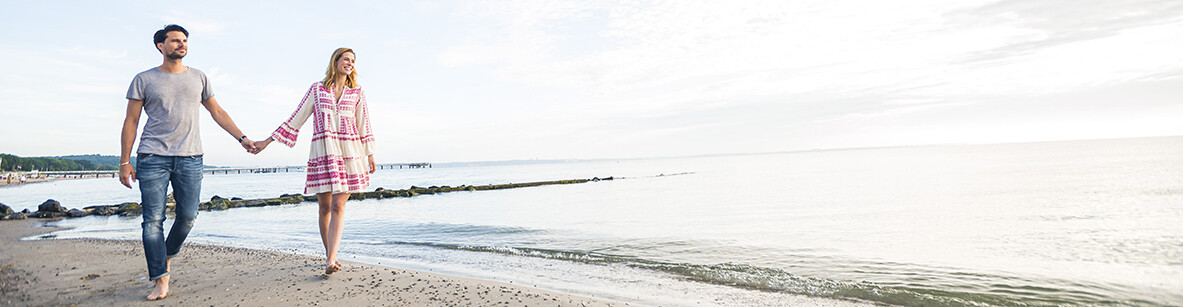 Pärchen spaziert barfuß händchenhaltend am Ostseestrand
