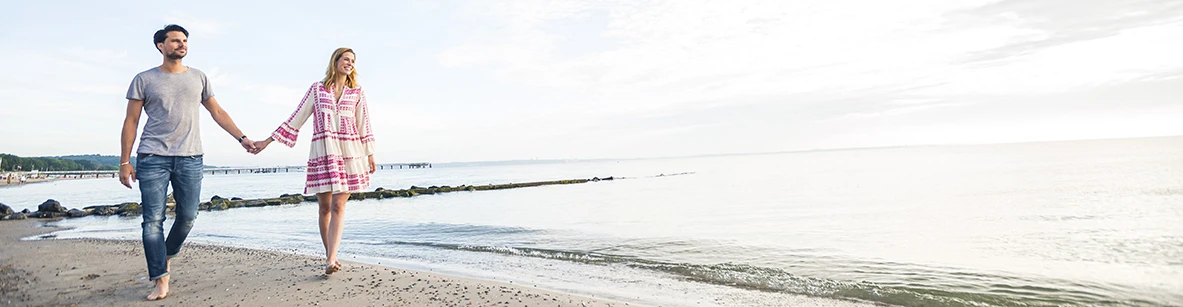 Pärchen spaziert barfuß händchenhaltend am Ostseestrand