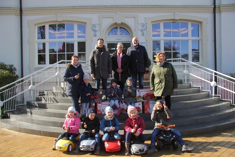 Gruppenfoto vor dem Rathaus mit Kindern auf Bobby Cars, die aussehen wie echte Autos