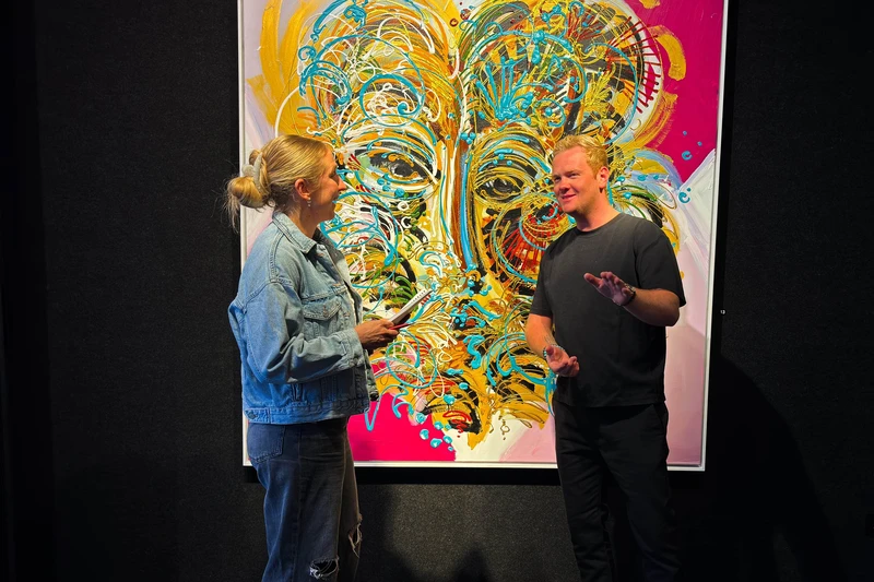 Lara Klewin und Künstler Leon Löwentraut unterhalten sich vor einem Bild vom Künstler. 
