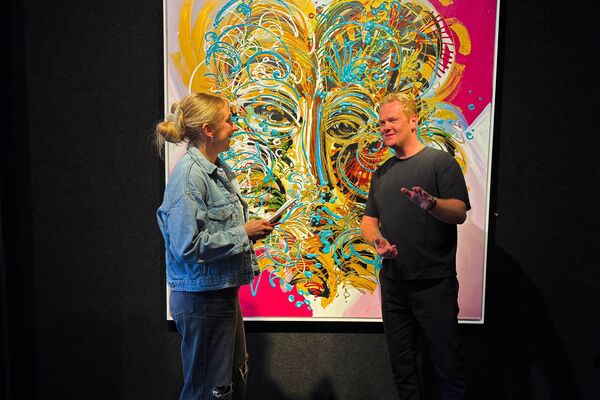 Lara Klewin und Künstler Leon Löwentraut unterhalten sich vor einem Bild vom Künstler. 