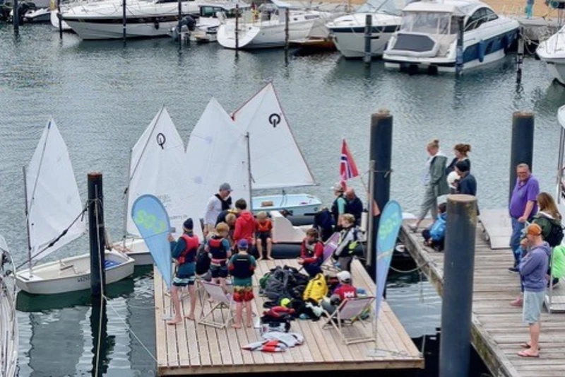 Kinder stehen auf einem Steg um sie herum sind viele kleine Segelboote.