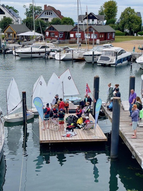 Kinder stehen auf einem Steg um sie herum sind viele kleine Segelboote.