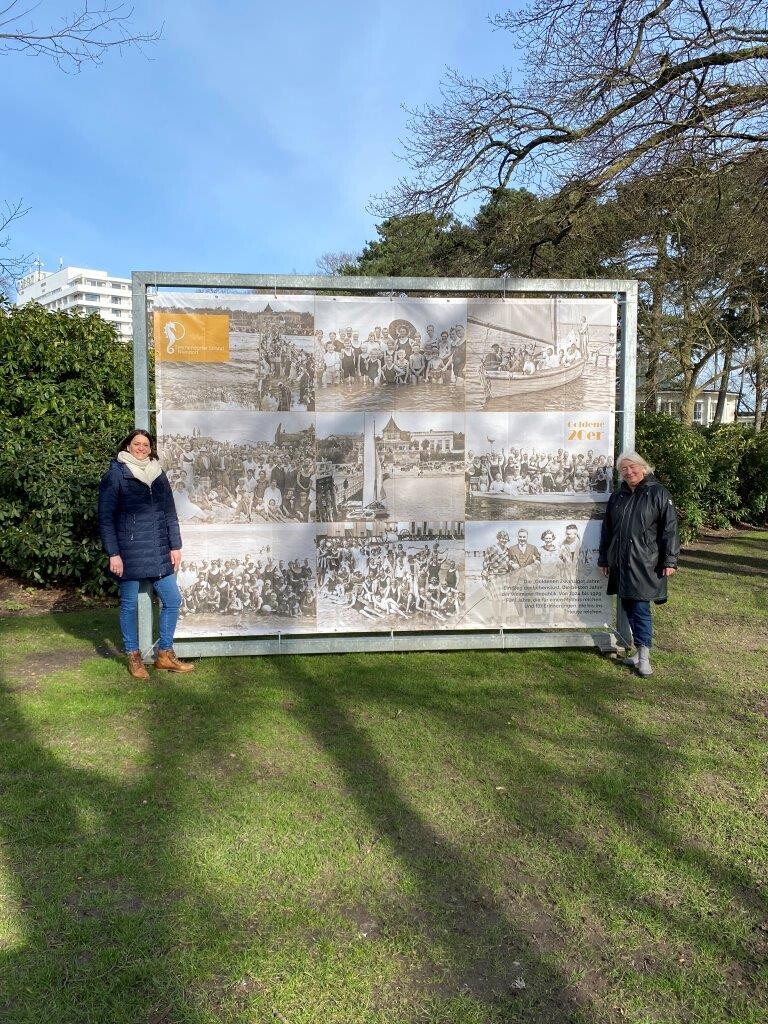 Silke Szymoniak und Stephanie Scheel vor einem Bild der "Goldenen Zwanziger" in einem Stahlrahmen