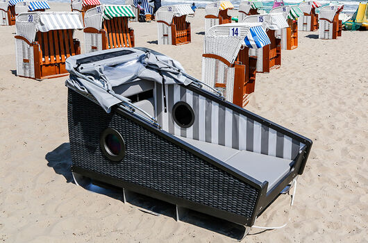Geöffneter Schlafstrandkorb inmitten von gewöhnlichen Strandkörben am Strand