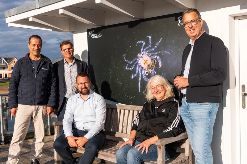 Vier Personen die auf einer Bank sitzen und in die Kamera schauen 