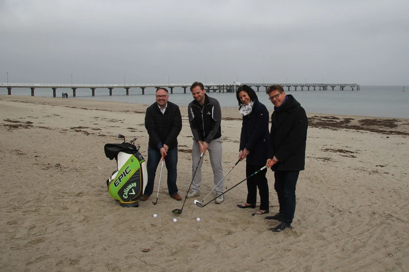 Vier Golfer mit Golfschlägern und Golfbällen am Strand