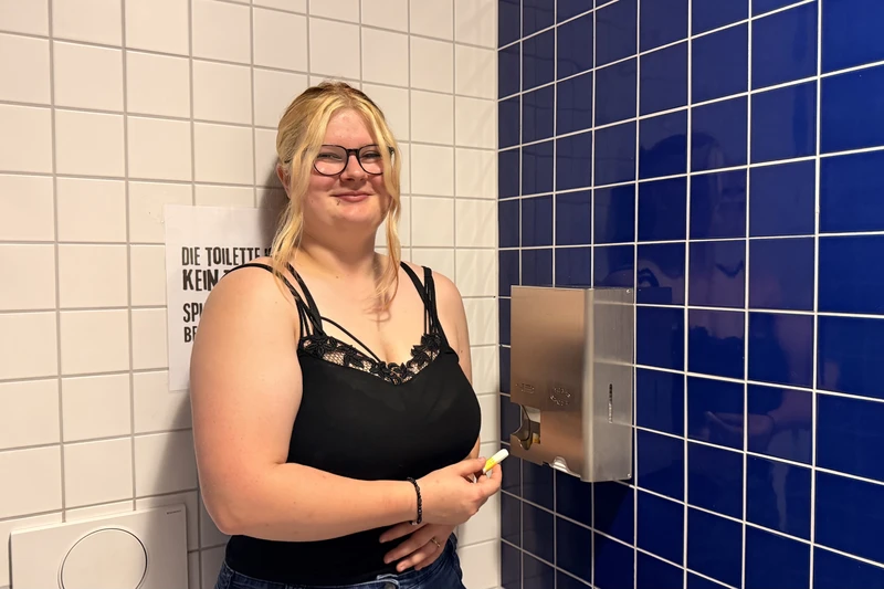 Ein Mädchen, was neben einem Spender steht und die ein Tampon in der Hand hält