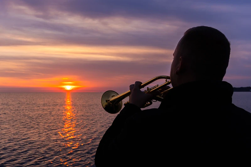 Mann mit Trompete beim Sonnenaufgang auf der Ostsee