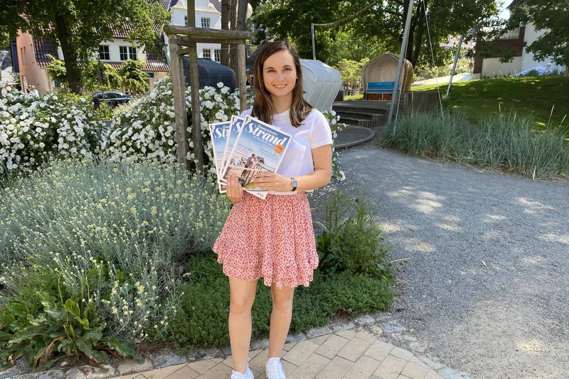 Eine Frau steht draußen im Grünen und hält mehrere Strandmagazine in den Händen