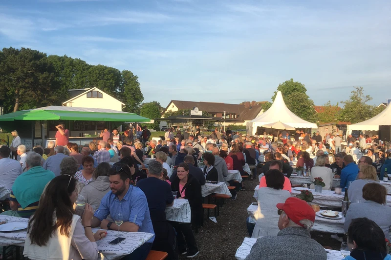 Viele Menschen sitzen draußen an Tischen