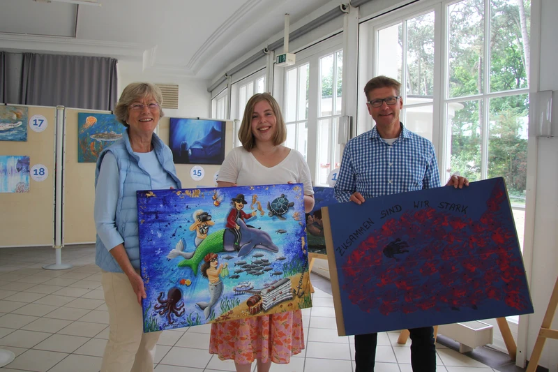 Drei Personen präsentieren zwei große Kunstwerke
