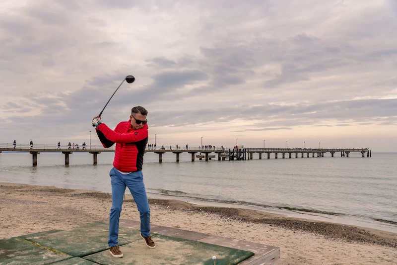 Ein Golfer holt aus um den Ball am Strand ins Wasser zu schlagen