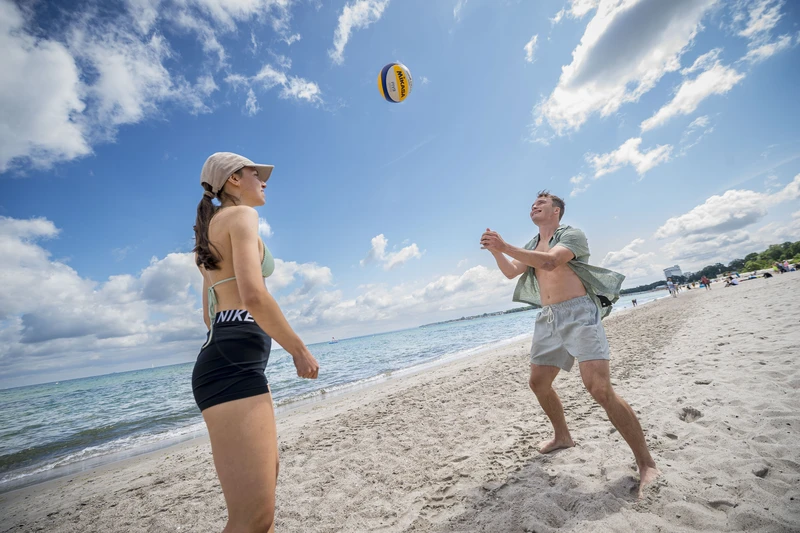 zwei Personen am Strand die einen Ball hochspielen 