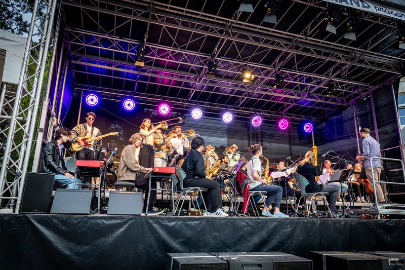 Musiker und Musikerinnen die auf der Bühne stehen die Instrumente spielen und singen 