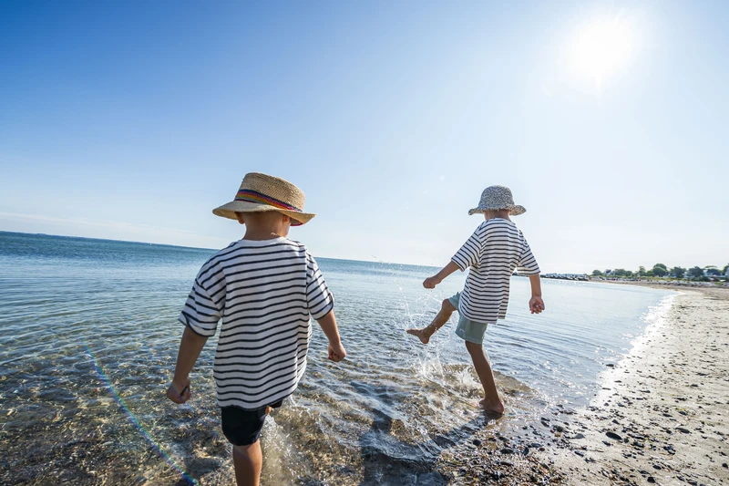 Zwei Kinder in gestreiften T-Shirts und mit Stoffhüten spielen im Wasser