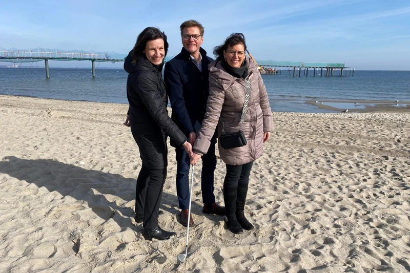 Zwei Frauen und ein Mann halten zusammen einen Golfschläger am Strand